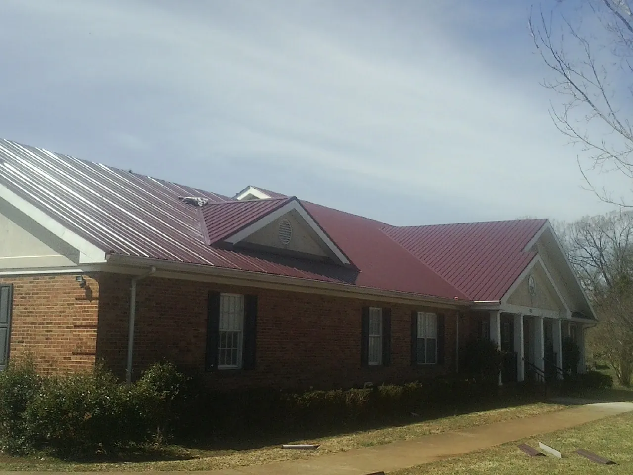 Red metal roof with gabled entries on a long brick building, from a Hail Damage Roof Repair job in Strathmere