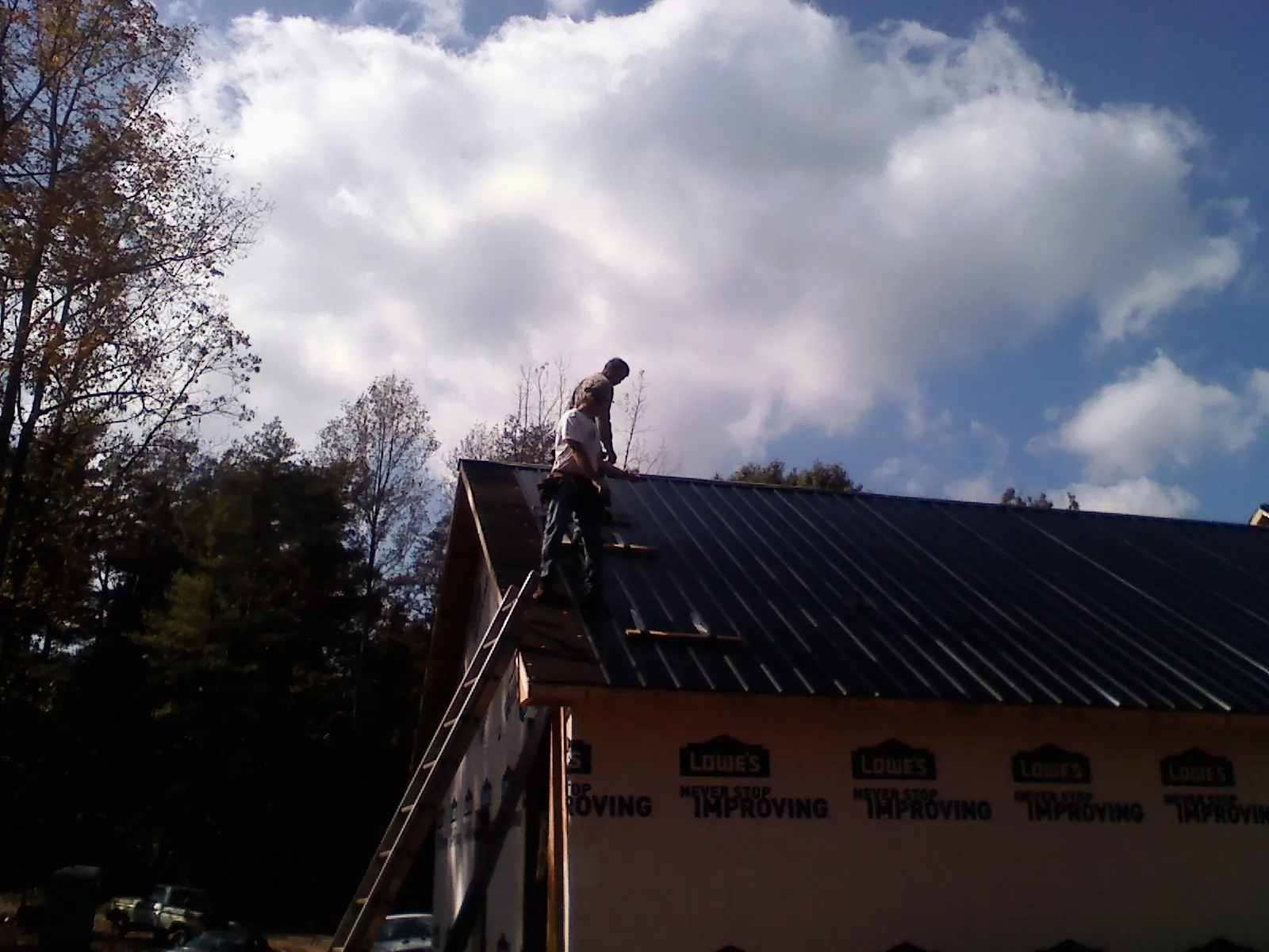 Roofer fastening dark metal panels high against a cloudy sky, from a Roof Inspection job in Strathmere