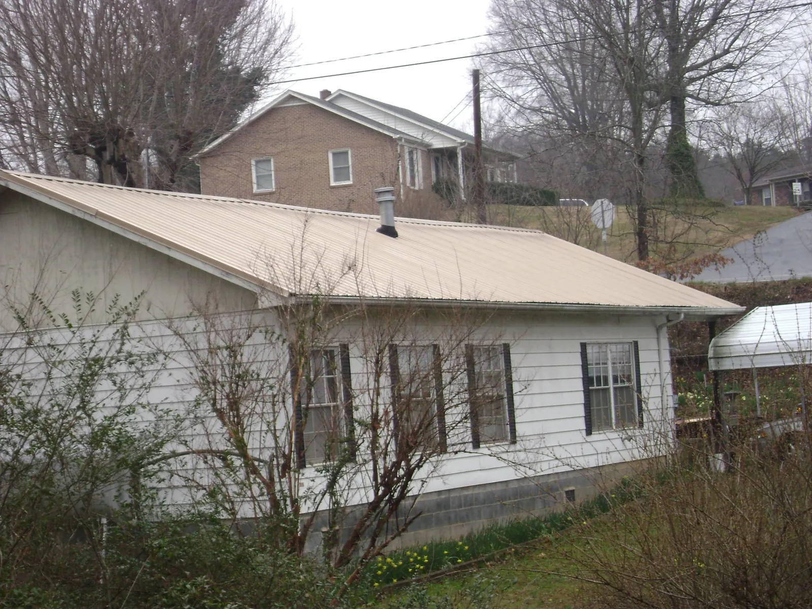 Tan metal roof on a white sided house set into a hillside — Commercial Roofing by Roofing Brothers in Strathmere